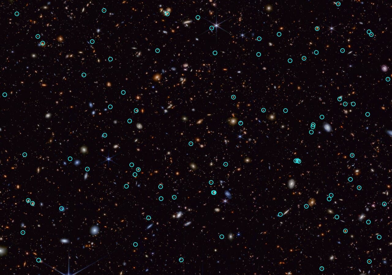 A dark field crowded with hundreds of small galaxies in white, orange and red, with dozens of tiny green circles scattered across it