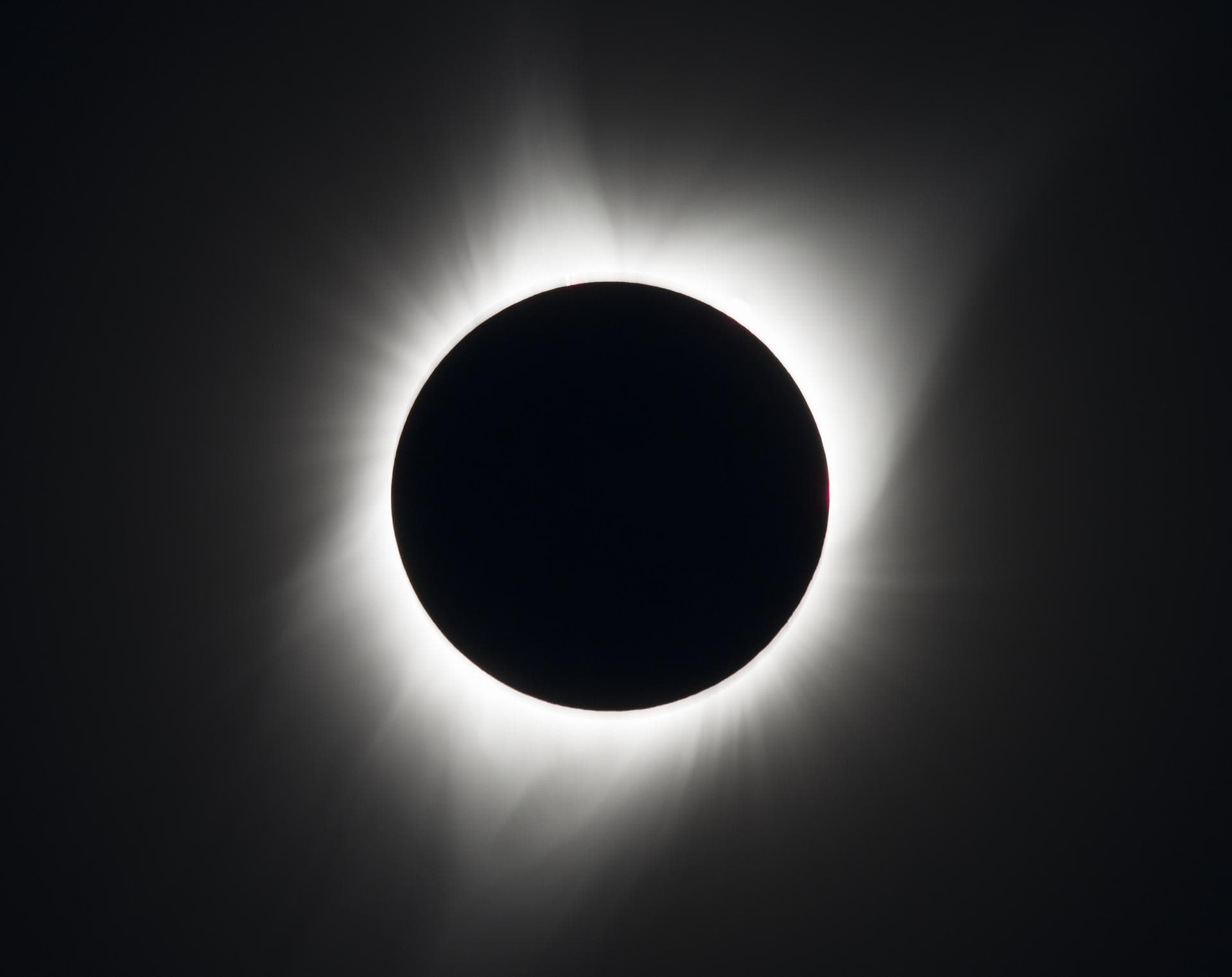 The black disk of the Moon covering the Sun, surrounded by a pale white halo against a dark sky