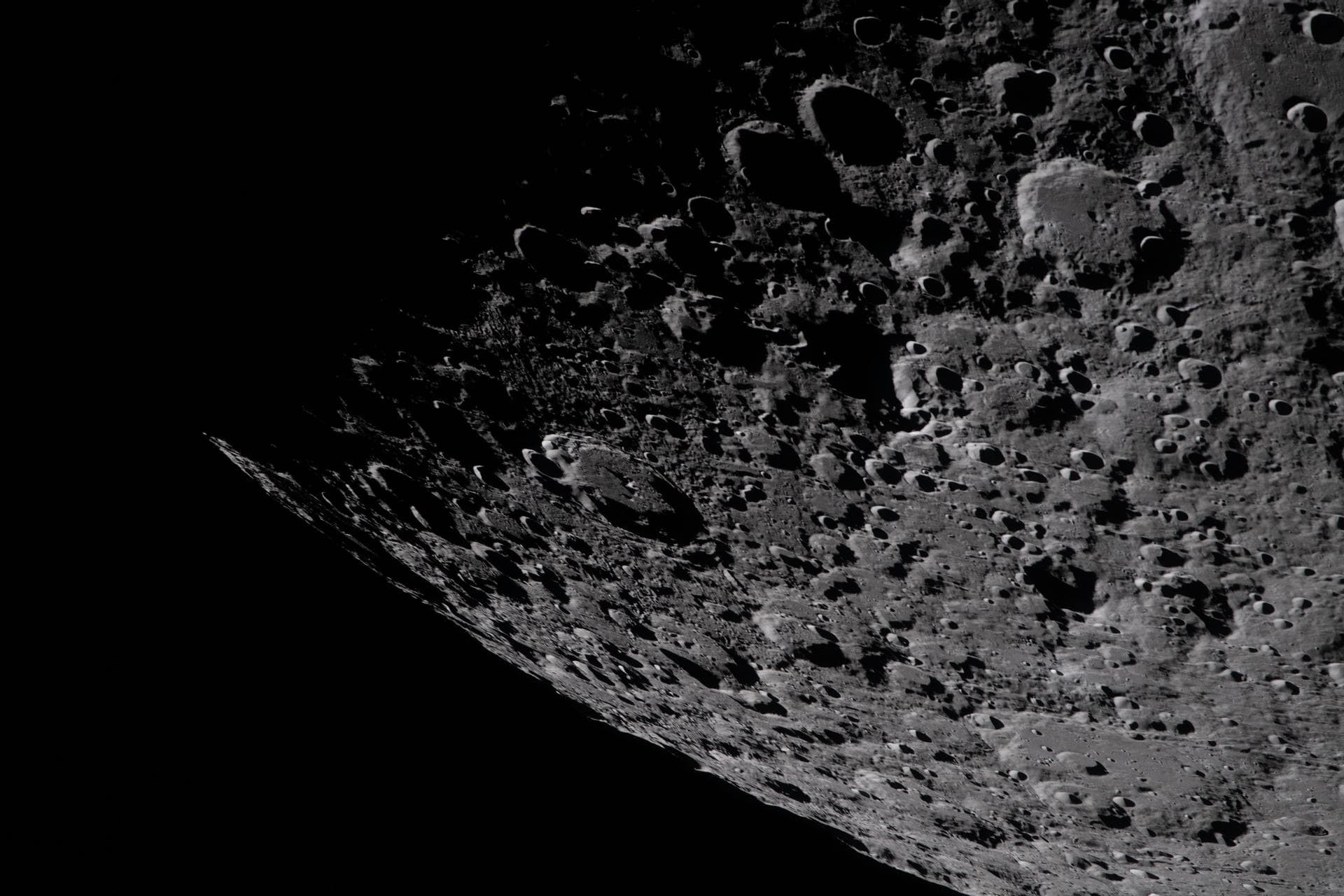 Gray lunar ground crowded with craters of every size, lit at a low angle, with a band of darkness across the top
