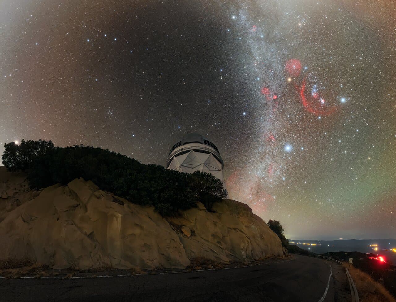 A large domed telescope building on a mountaintop at night, with the bright band of the Milky Way rising behind it