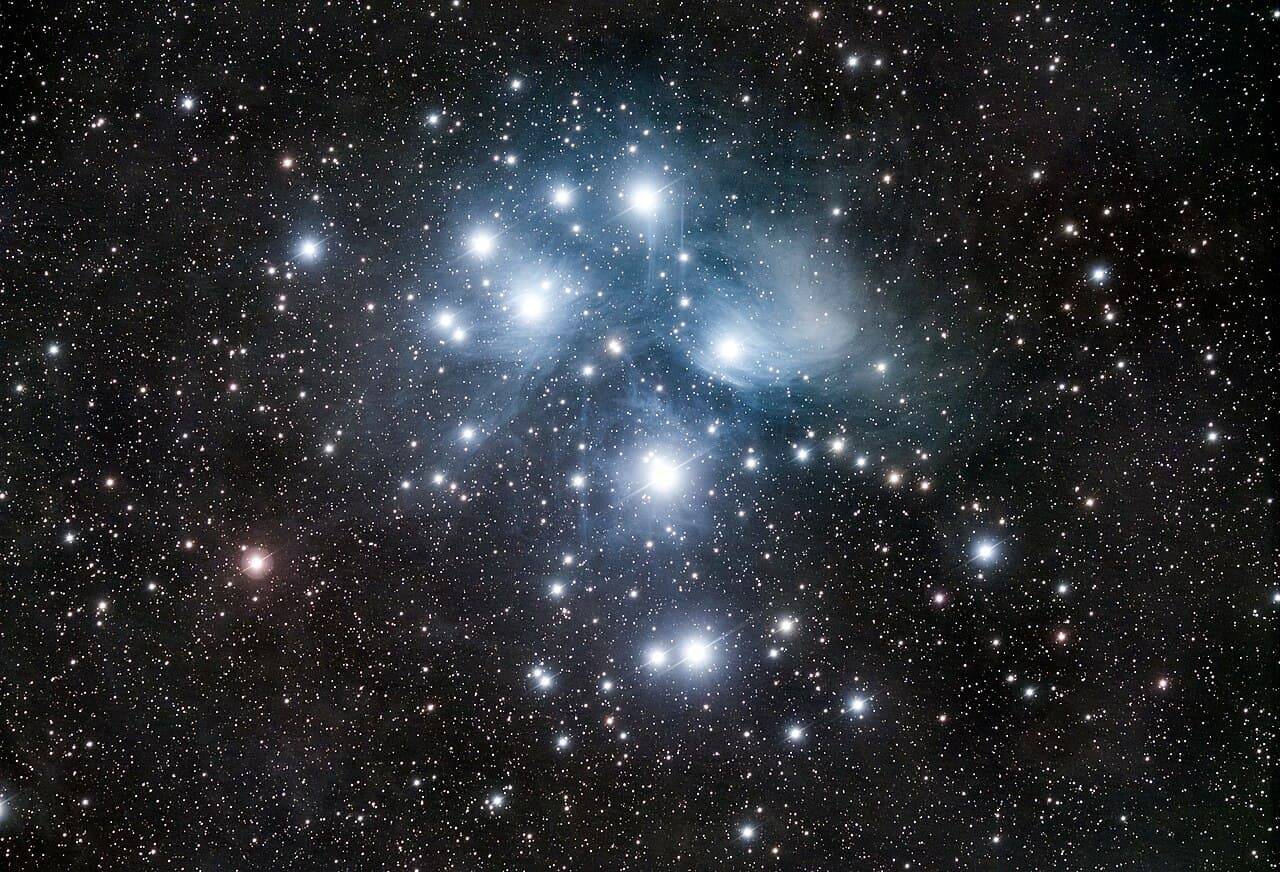 A dense field of stars with a handful of bright blue-white stars at the center, wrapped in pale blue haze